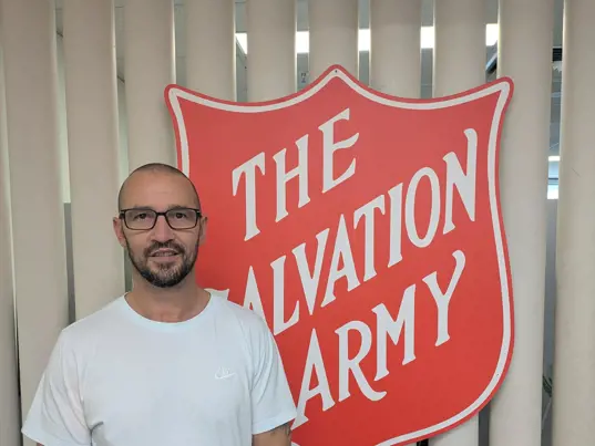 Natham standing in front of The Salvation Army shield logo.
