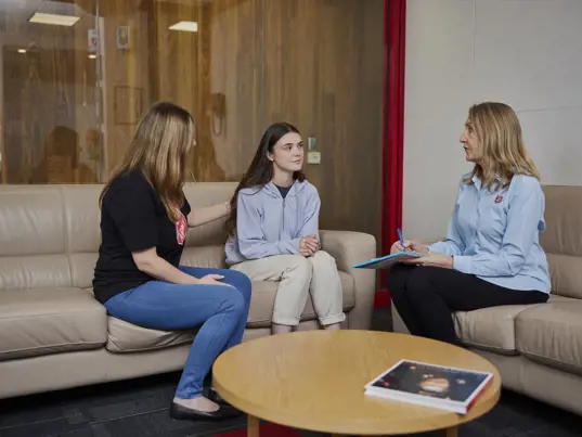 A young woman, flanked by two Salvation Army workers, engages in a supportive conversation.