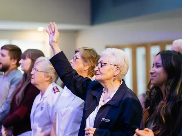 A woman holds a hand to the sky as people gather together during a church service.