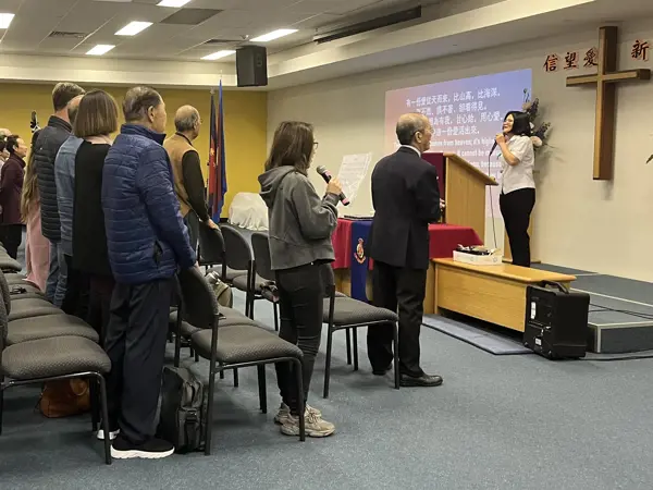People standing in worship while listening to the Corps Officer at the front of the worship hall.