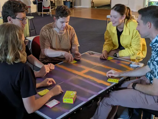 A group of young adults sitting around a table and playing a card game.