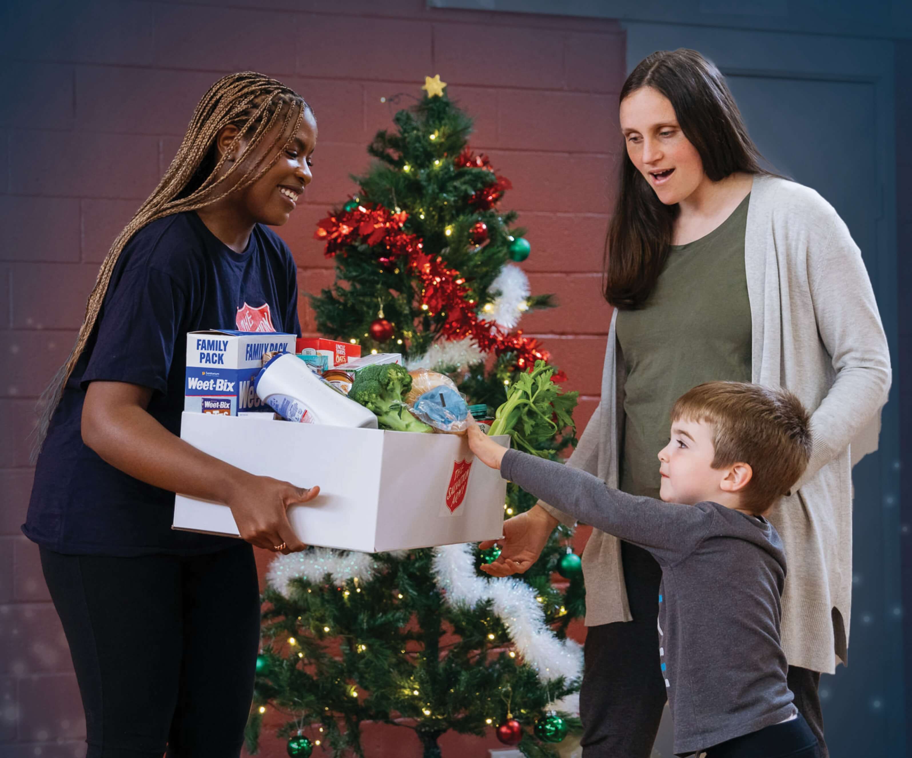 A Salvos Christmas Volunteer hands a Christmas hamper to a mother and her son. 