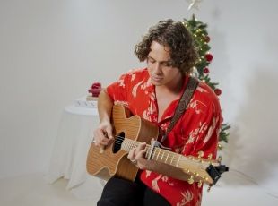 Home and Away actor and musician Matt Evans performing a Christmas song in a studio with an acoustic guitar. 