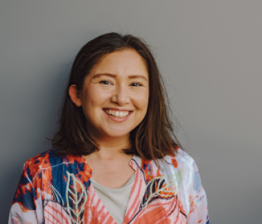 A woman wearing a floral shirt smiles warmly, radiating joy and positivity in her expression.