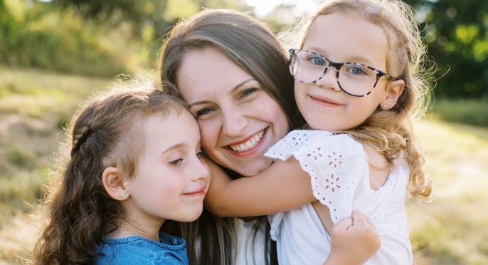 A young mother is hugged by her two daughters.