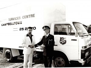 Salvation Army officer shaking a man's hand in front of a truck.