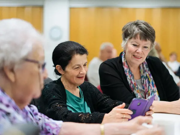 A diverse group of older community members enjoying fellowship and share photos on their phones..